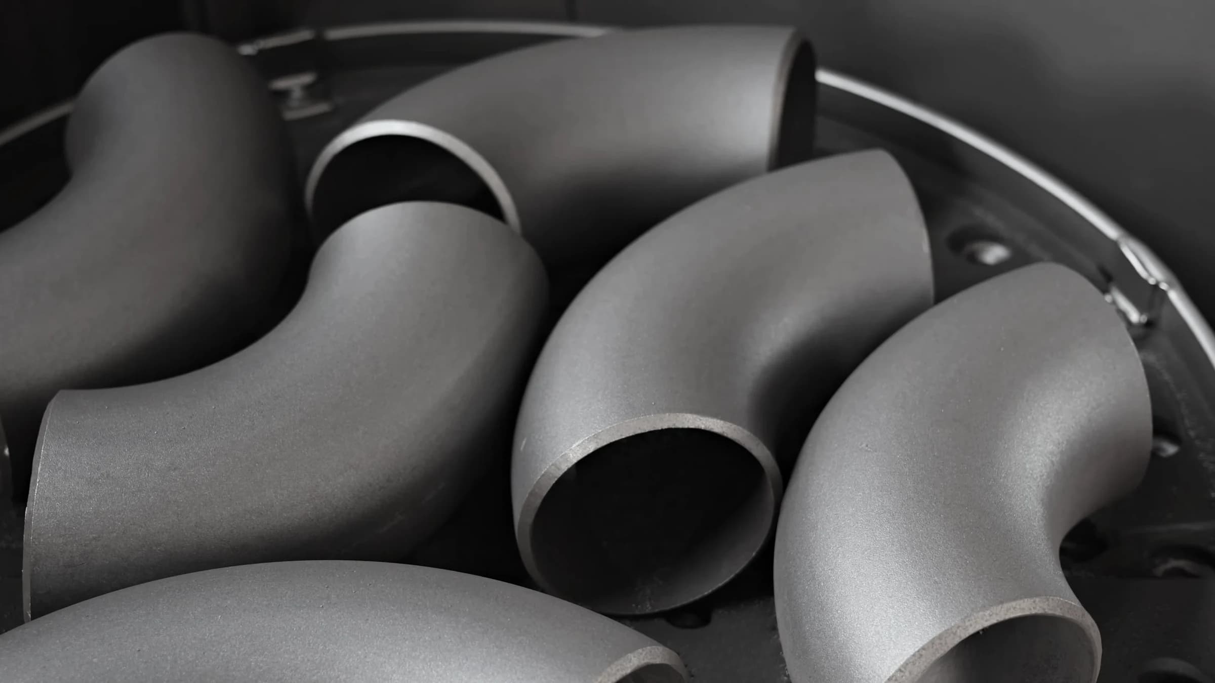 Shot-blasted carbon-steel elbows with an even, matte finish on the blasting turntable
