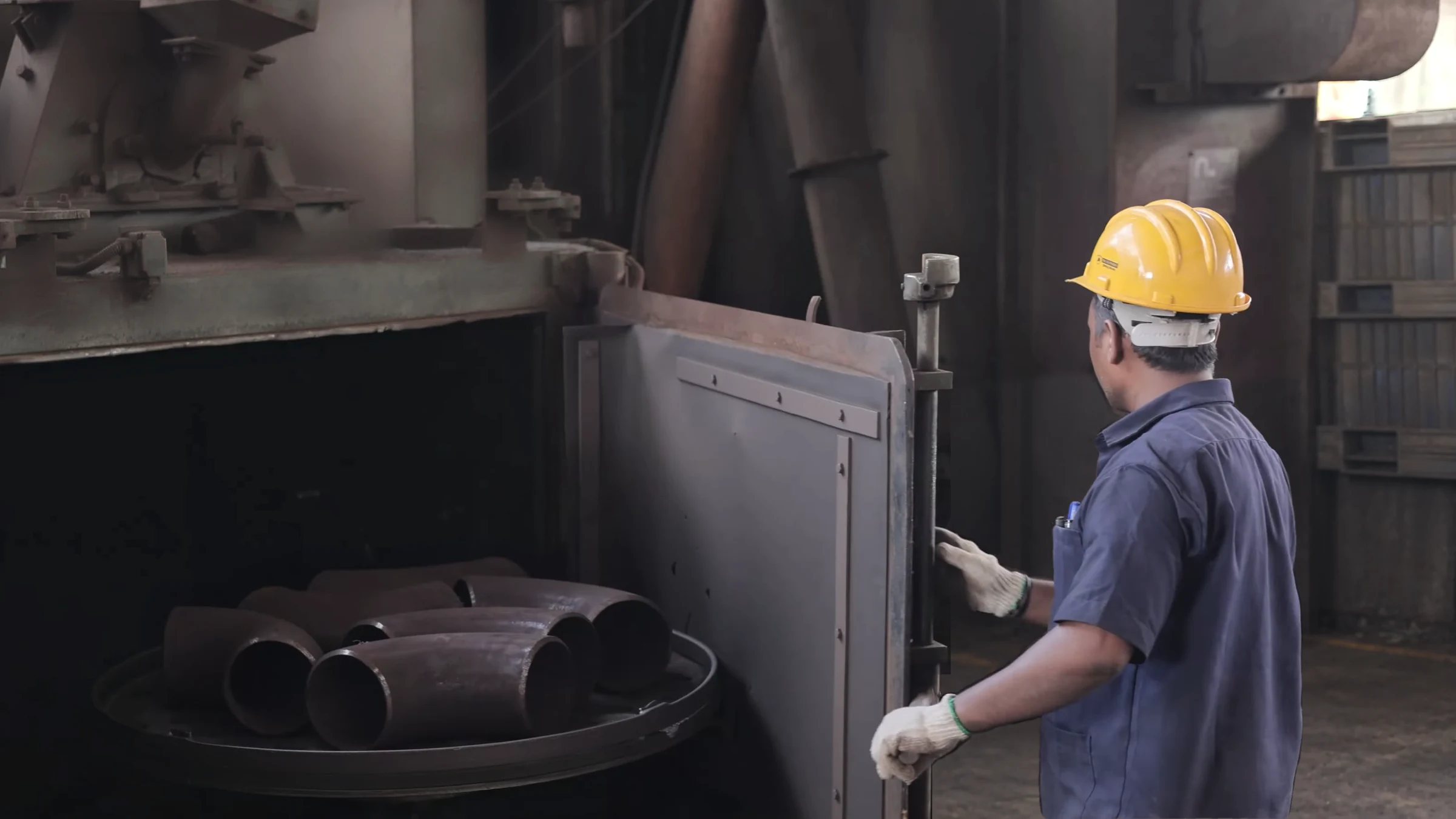 Operator in a safety helmet and gloves loading elbows into the shot blasting machine