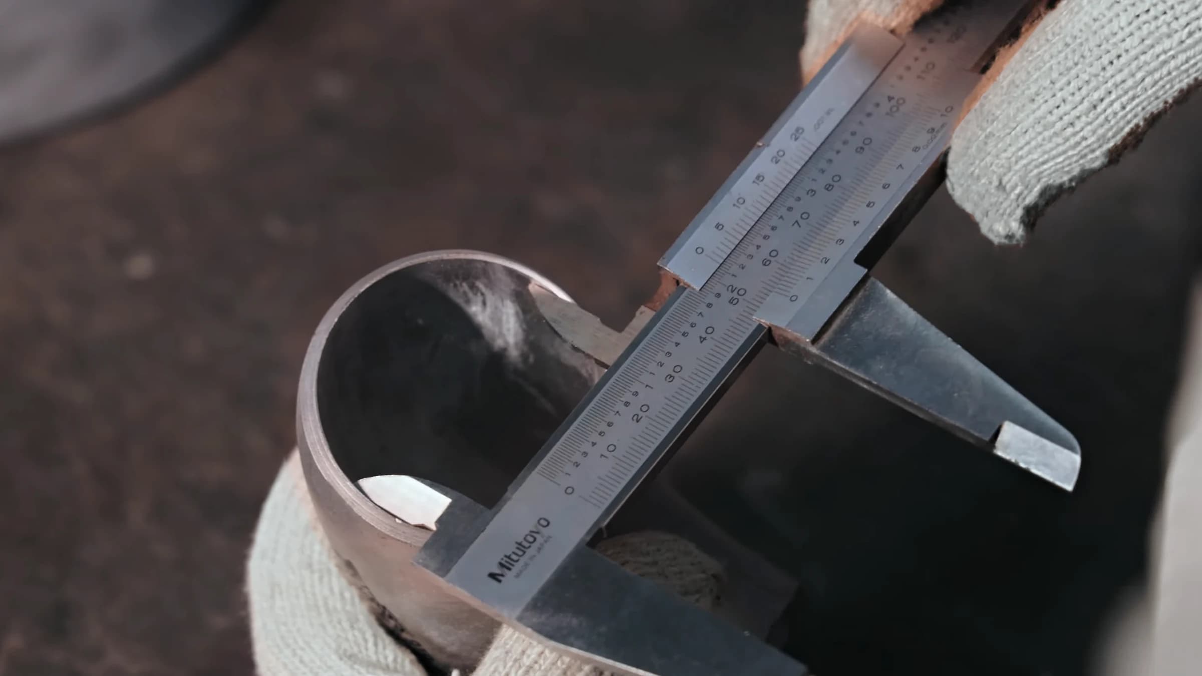 Gloved hands measuring a stainless-steel elbow with a Mitutoyo vernier caliper