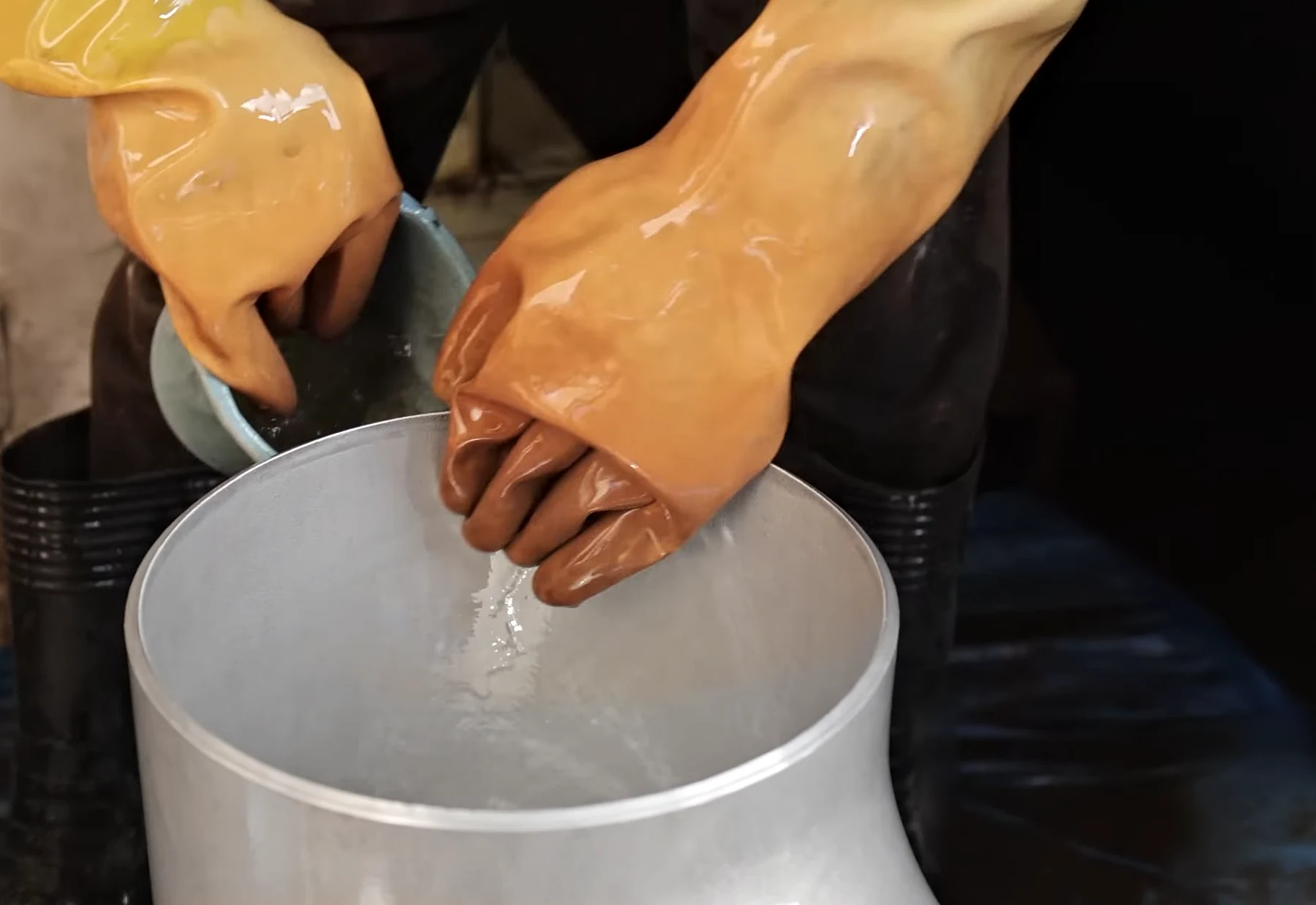 Hands in long rubber gauntlets rinsing a large stainless-steel tee after pickling