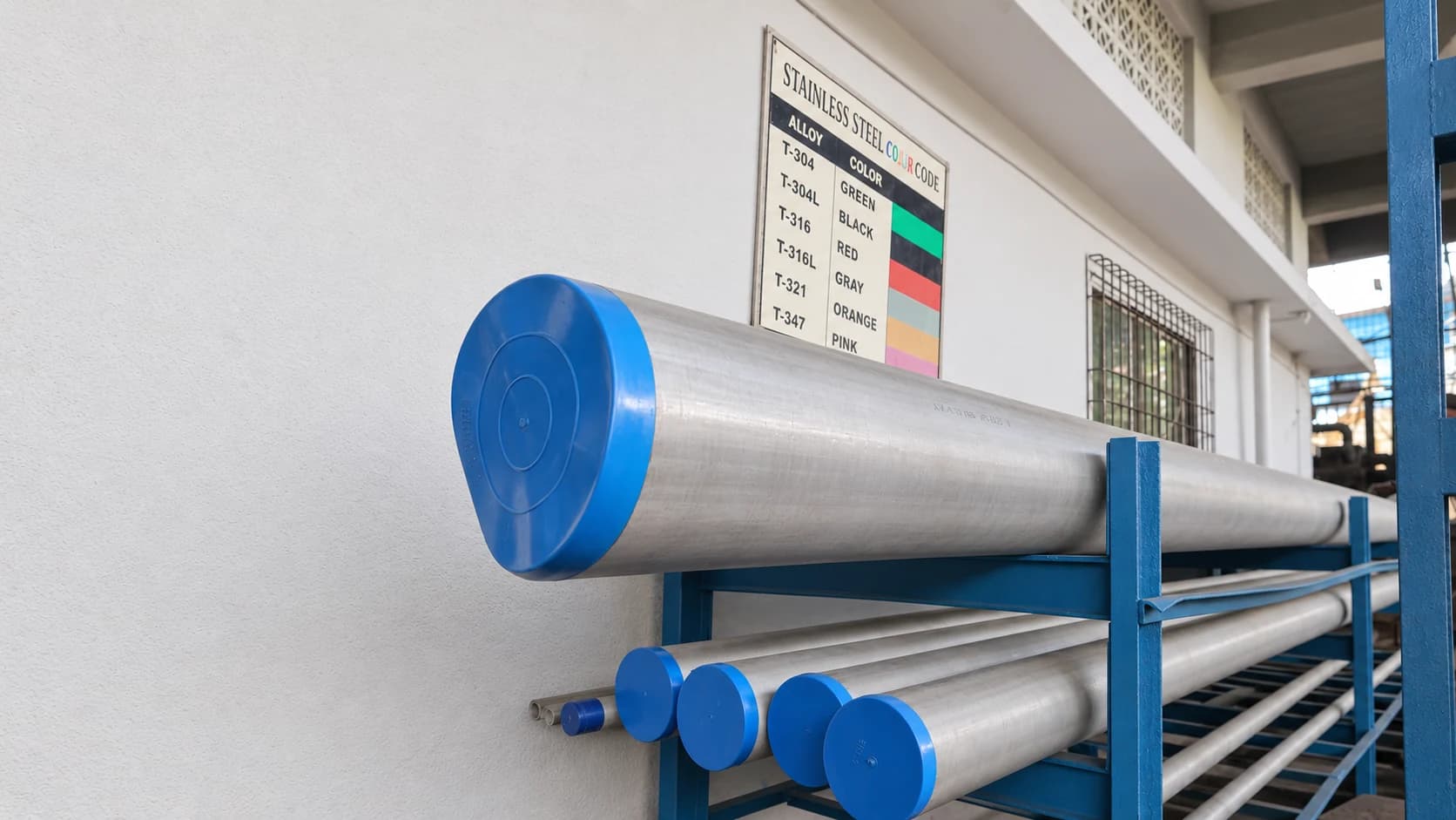 Stainless-steel pipe with blue end caps on a blue rack beneath a stainless-steel colour-code chart