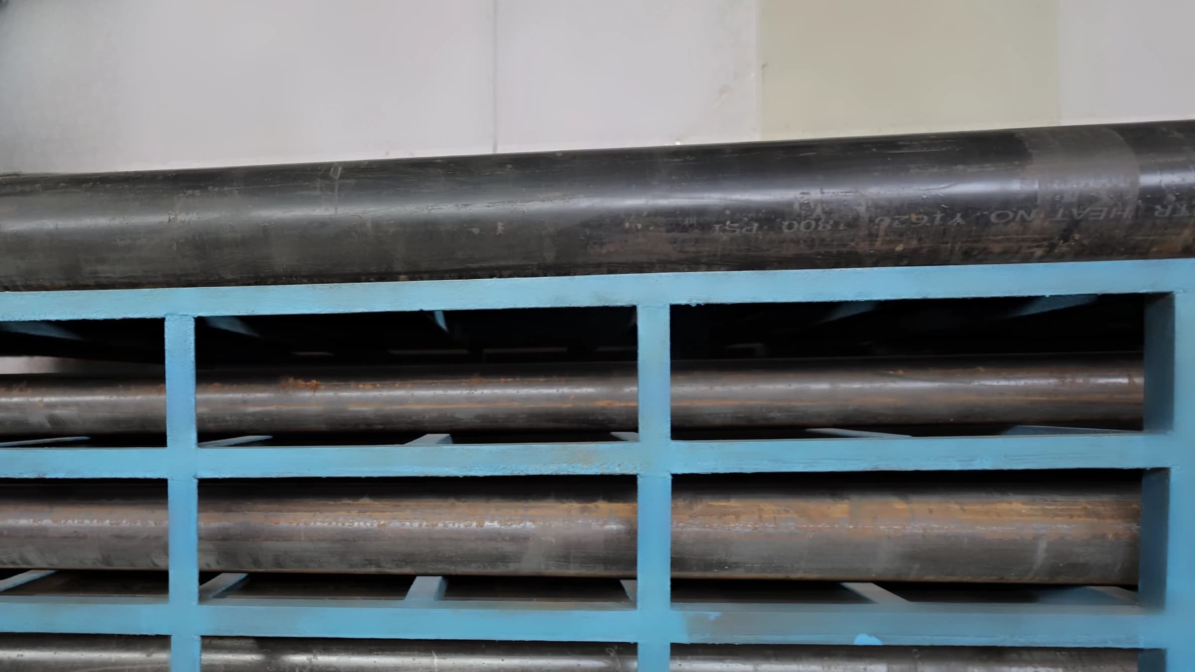 Carbon-steel pipe on a blue steel rack, a heat number stencilled on the top pipe