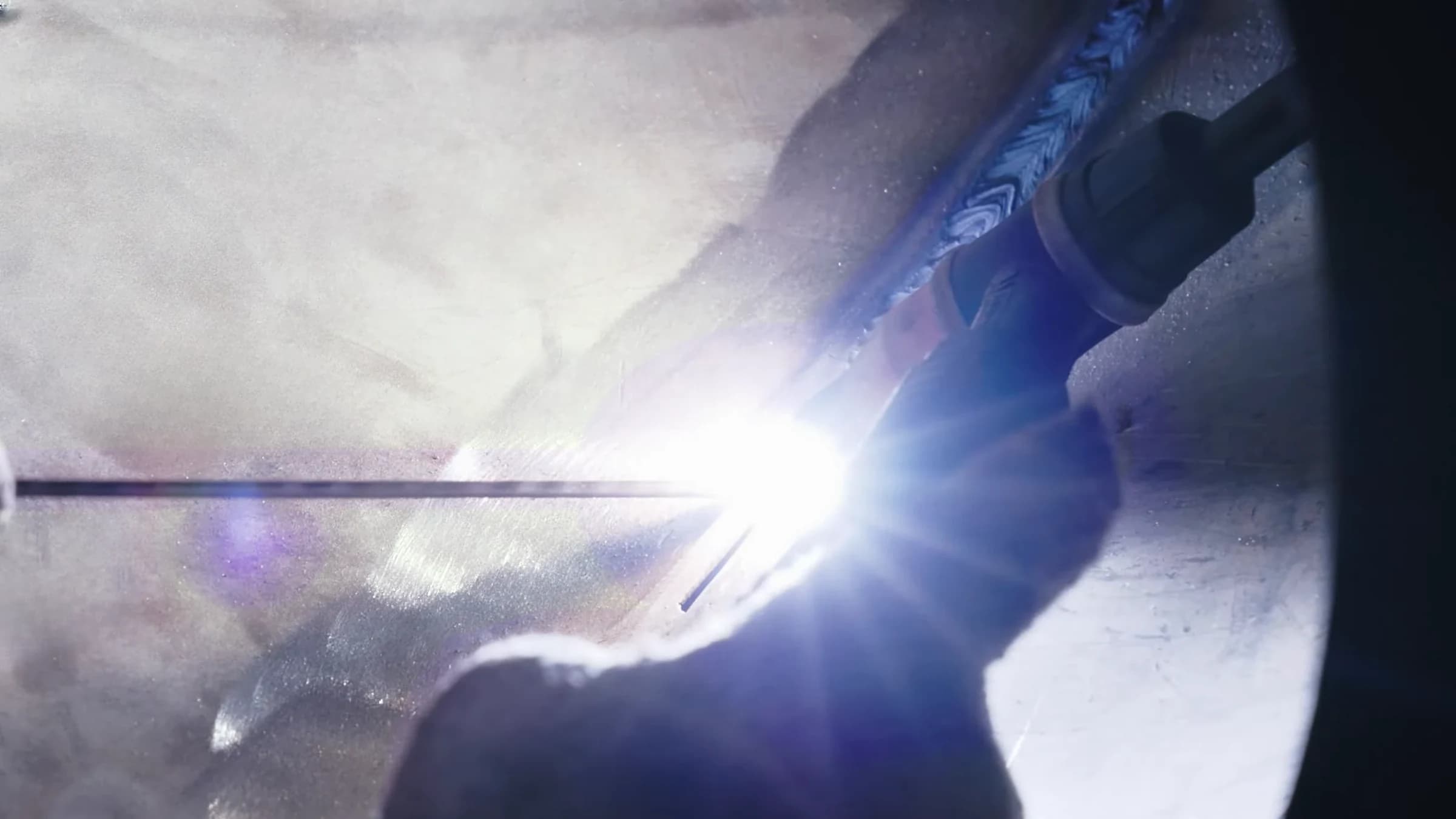 Gloved welder feeding filler rod into a TIG arc on a large stainless-steel fitting